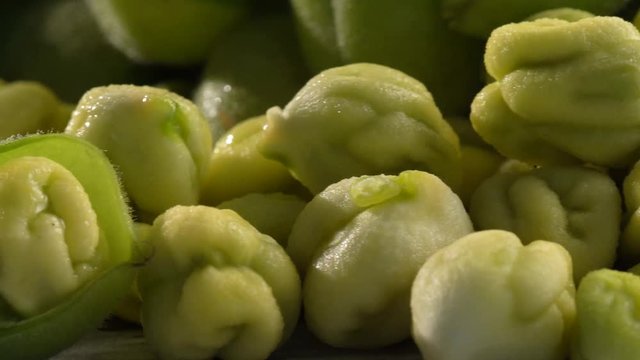 Extreme closeup slider to the right of moist, raw, uncooked chickpeas in and out of their husk on a white rustic table.