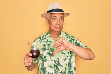 Middle age senior grey-haired man wearing summer hat drinking traditional mate drink with angry...