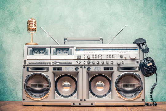 Retro old ghetto blaster stereo radio cassette tape recorder boombox from circa 80s, golden microphone, headphones front concrete wall background. Nostalgic music concept. Vintage style filtered photo