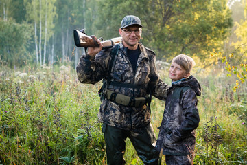 Father teaching his son about gun safety and proper use on hunting in nature.