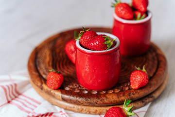 fresh strawberries in red pots on a wooden background, on a drop of water berries. healthy nutrition, vitamin charge, summer berries