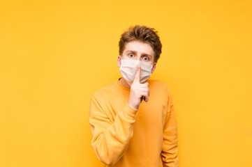 Surprised young man in a medical protective mask, shows a finger to lips gesture 