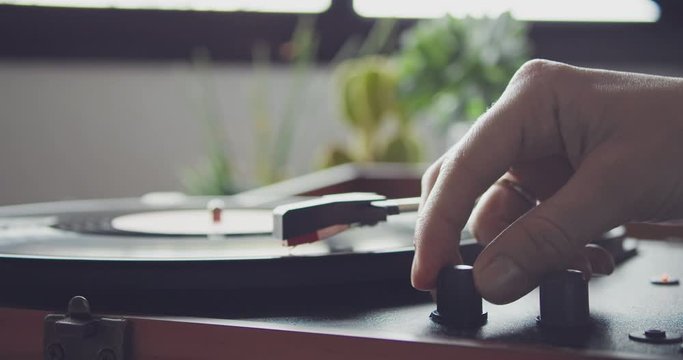 Female hand raising the volume tumbler on vintage portable record player and start paying vynil record