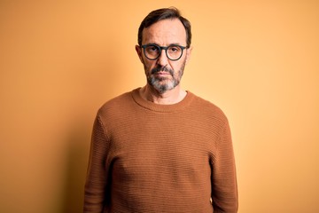 Middle age hoary man wearing brown sweater and glasses over isolated yellow background Relaxed with serious expression on face. Simple and natural looking at the camera.