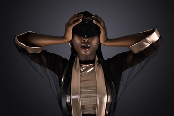 A gorgeous young black female posing by herself wearing a golden top, a shear sexy black kimono and a black head piece covering her eyes.