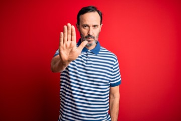 Middle age hoary man wearing casual striped polo standing over isolated red background doing stop...