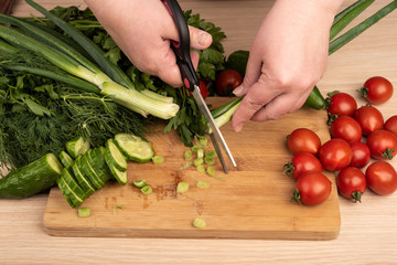 Woman cuts green onion with scissors over a cutting board.