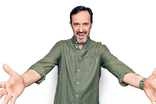 Middle age handsome man wearing casual green shirt over isolated white background looking at the camera smiling with open arms for hug. Cheerful expression embracing happiness.