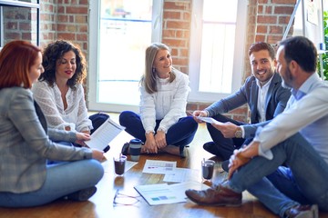Group of business workers smiling happy and confident. Sitting on the floor relaxed working together speaking and reading documents at the office