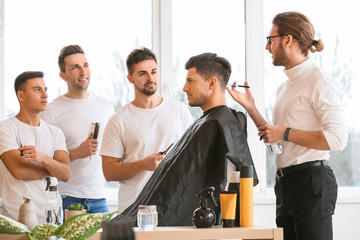 Professional hairdresser teaching young men in salon