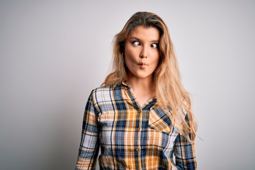 Fototapeta premium Young beautiful blonde woman wearing casual shirt standing over isolated white background making fish face with lips, crazy and comical gesture. Funny expression.