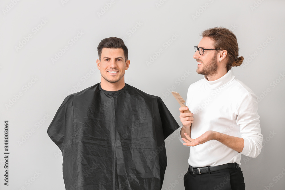 Wall mural Young hairdresser working with client against white background