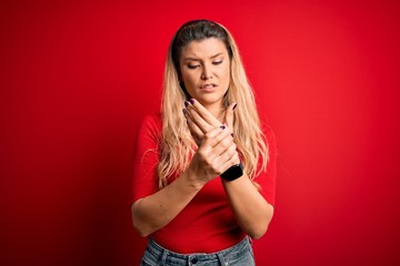 Young beautiful blonde woman wearing casual t-shirt standing over isolated red background Suffering...
