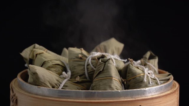 Cooking zongzi - Steamed Chinese rice dumpling in a steamer, fresh prepared food for Dragon Boat Duanwu Festival isolated on black background, close up lifestyle.
