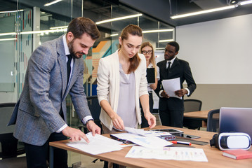 Slow motion of handsome enterprising bearded businessman standing near boardroom table with his attentive female colleague and explaining the reports data