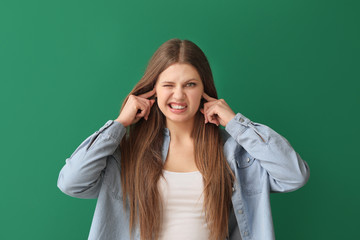 Young woman suffering from loud noise on color background