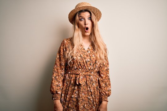 Young beautiful blonde woman wearing summer dress and hat over isolated white background afraid and shocked with surprise expression, fear and excited face.