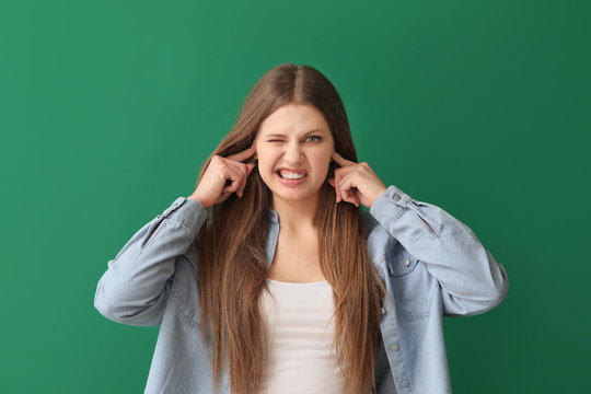 Young Woman Suffering From Loud Noise On Color Background
