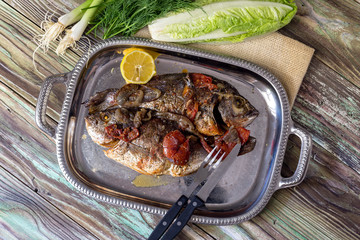 The gilt-head bream (Sparus aurata) with vegetables on a plate close-up