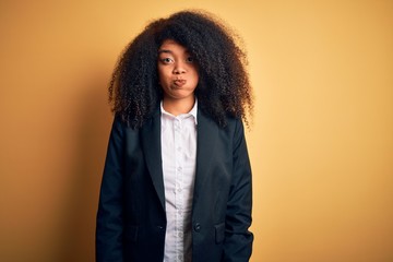 Young beautiful african american business woman with afro hair wearing elegant jacket puffing cheeks with funny face. Mouth inflated with air, crazy expression.