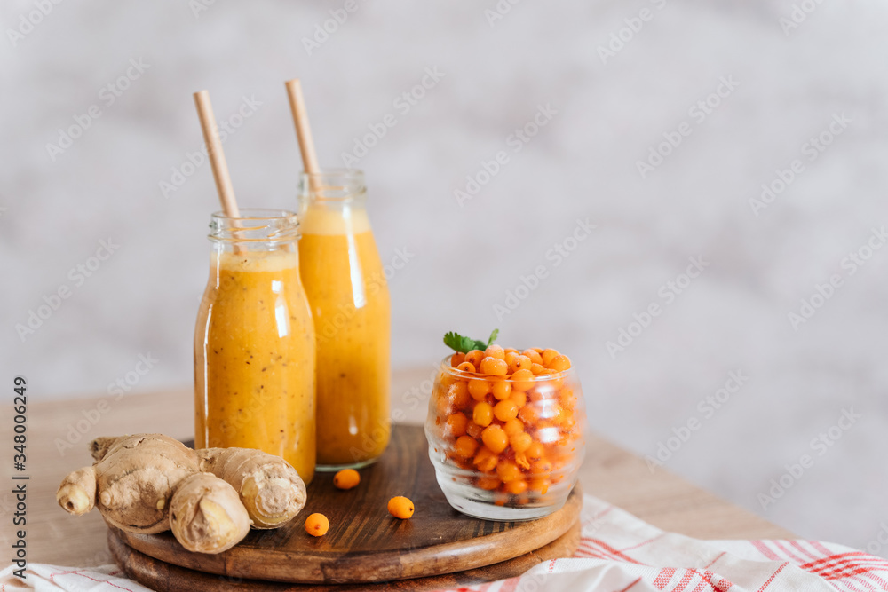 Wall mural Bright sea buckthorn smoothie on a rustic board. berries, ginger, glass bottles, paper tubes. no plastic. healthy food