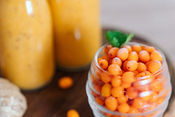 Bright sea buckthorn smoothie on a rustic board. berries, ginger, glass bottles, paper tubes. no plastic. healthy food. Frozen berries