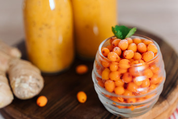 Bright sea buckthorn smoothie on a rustic board. berries, ginger, glass bottles, paper tubes. no plastic. healthy food