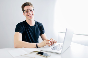 Student with his computer working from home during confinement, he is looking at camera and smiling