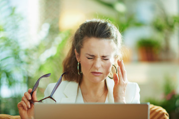 tired young woman with laptop and glasses having eye pain