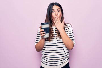 Young beautiful brunette woman drinking cup of takeaway coffee over isolated pink background covering mouth with hand, shocked and afraid for mistake. Surprised expression