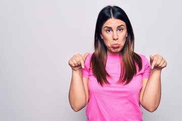 Young beautiful brunette woman wearing casual pink t-shirt standing over white background Pointing down looking sad and upset, indicating direction with fingers, unhappy and depressed.