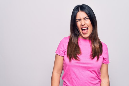 Young beautiful brunette woman wearing casual pink t-shirt standing over white background winking looking at the camera with sexy expression, cheerful and happy face.
