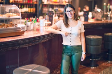 Young beautiful woman smiling happy and confident. Standing with smile on face leaning on the counter bar at restaurant