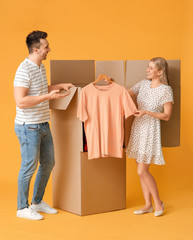 Young couple unpacking clothes on color background