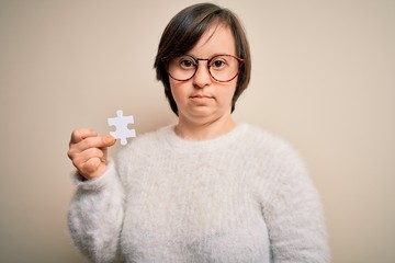 Young down syndrome woman holding puzzle piece as problem solution and cooperation union with a confident expression on smart face thinking serious