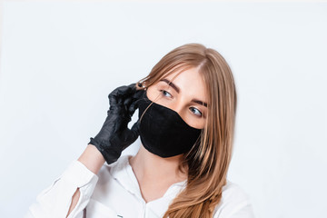 Doctor in a white suit and medical mask, holding hands in black gloves and thinking about the consequences of the coronavirus epidemic. Doctor on a white background. The doctor puts on a black mask.