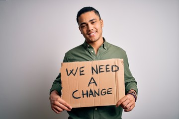 Young brazilian activist man asking for change holding banner over white background with a happy face standing and smiling with a confident smile showing teeth