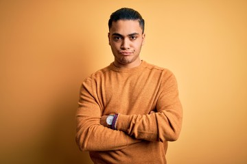 Obraz premium Young brazilian man wearing casual sweater standing over isolated yellow background skeptic and nervous, disapproving expression on face with crossed arms. Negative person.