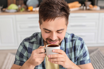 Young man drinking hot coffee in kitchen