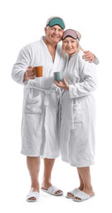 Mature couple in bathrobes and with sleep masks drinking tea on white background