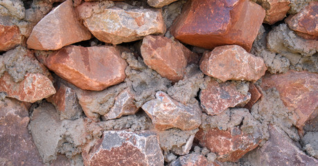 Wall of large rubble for backdrop. Pieces of stones in a cement mortar. Colors are gray, orange, red.