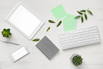 Tablet computer, mobile phone, PC keyboard and stationery on white wooden background