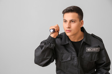 Male security guard with flashlight on grey background