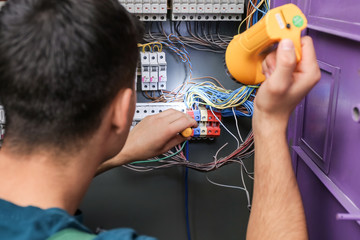 Male electrician with flashlight repairing distribution board