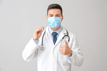 Male doctor with flashlight showing thumb-up gesture on grey background