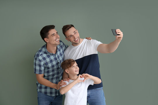 Happy Gay Couple With Adopted Child Taking Selfie On Color Background