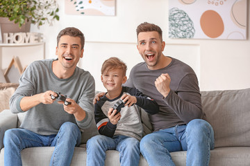 Happy gay couple with adopted child playing video game at home