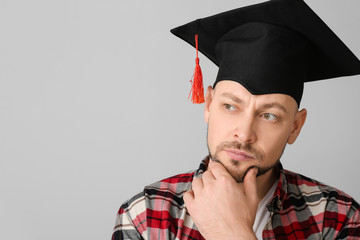 Thoughtful man in graduation hat on grey background