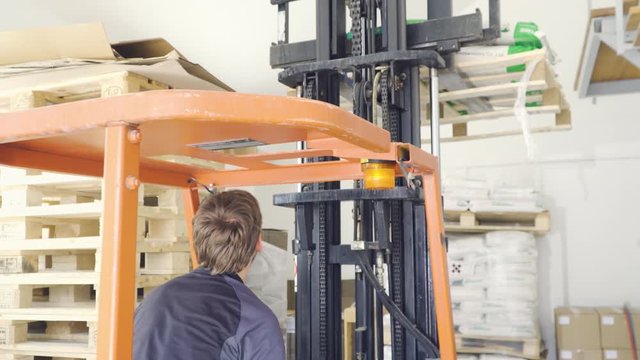 Young caucasian
man industrial worker operating and driving forklift, unloading pallets. 
