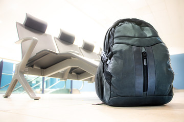 The backpack stands on the floor in front of a row of empty seats in an airport terminal. Airport interior without people.